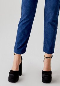 Tacchi a piattaforma neri con un tacco spesso e punta aperta. Accompagnati da pantaloni blu a vita alta con una texture liscia e design affusolato.