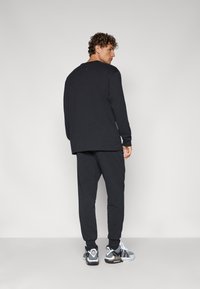 Black long-sleeve shirt and matching jogger pants, made of soft fabric, featuring a relaxed fit. Sneakers with a black and white design complete the look.