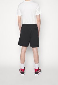 Svarta träningsshorts med resårmidja, sidofickor och rundade fållar, kombinerade med en enkel vit t-shirt och färgglada högstövlar.