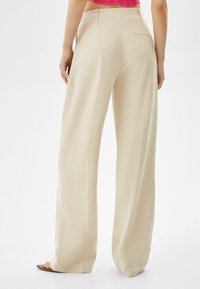 Beige vida byxor med en slät textur, med fickdetaljer och en ren silhuett, bärs med en rosa kortärmad topp.