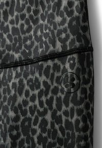 Legíny s leopardím vzorom v čiernej a sivej farbe, vyrobené z hladkej, elastickej látky s čiernym prešívaním a okrúhou nášivkou.