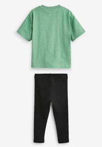 Grünes Kurzarmhemd mit Rundhalsausschnitt und texturiertem Finish, kombiniert mit schwarzen dehnbaren Leggings, beide aus weichem Baumwollmaterial.