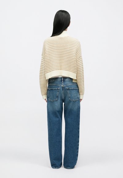 Cardigan scurt din tricot crem cu model texturat, asortat cu blugi largi albaștri, cu buzunare în partea din spate și croială dreptă.