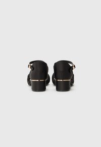Sorte ankelrem-sandaler med en glattet overflade, med en liten blokkheel og gullfarget accent nær basen. Åpen bakdesign.