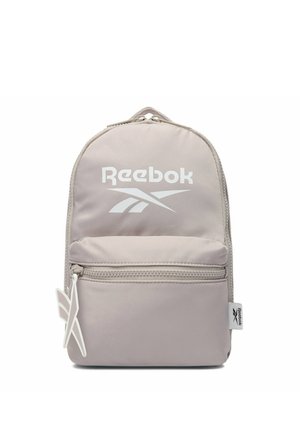 Jasnobeżowy plecak Reebok z przednią kieszenią na zamek, białym logo na głównej komorze oraz firmowym suwakiem i boczną metką.