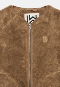 Καφέ φλις ζακέτα με φερμουάρ σε ασημί απόχρωση και μικρή τετράγωνη ετικέτα λογότυπου στο στήθος, χωρίς γιακά, και με ορατή ετικέτα μάρκας στο εσωτερικό.