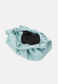 Jasnozielona torebka typu scrunch z marszczonym górnym brzegiem, wyposażona w czarne wnętrze o subtelnym połysku. Zabezpieczona zatrzaskiem.
