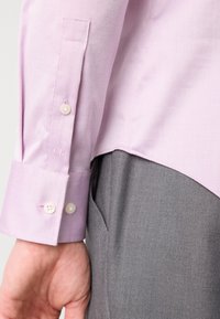 Hellpurpurnes Langarmshirt mit geknöpften Bündchen, das eine glatte Textur, einen subtilen Glanz und ein kleines, auf dem Ärmel gesticktes "CK"-Logo aufweist.