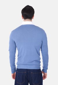 Maglione azzurro chiaro con colletto e polsini a costine, tessuto lavorato a maglia, design aderente, indossato sopra una camicia bianca con colletto, abbinato a jeans blu scuro.