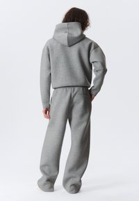 Gray cotton hoodie with a large hood, paired with matching loose-fit sweatpants featuring an elastic waistband and back pocket.