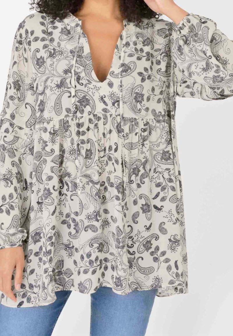 Blusa leggera in crema con motivo paisley nero, scollatura a V e vita arricciata. Presenta maniche lunghe e vestibilità ampia.