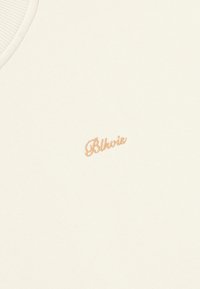 Crème kleurige tanktop met ribbelachtige halslijn en geborduurd "Blkvis" logo in een zachte oranje tint aan de rechterkant. Soepele textuur.