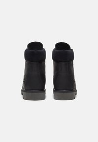 Mustad mustad mustad, millel on sametist krae, pehmendatud ülemine osa ja tekstureeritud kummitald. Küljel on metallist aksent.