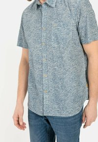 Camisa de manga corta en azul claro con patrón de olas, con botones en la parte delantera, cuello y bolsillo en el pecho. Fabricada con un tejido de textura suave.