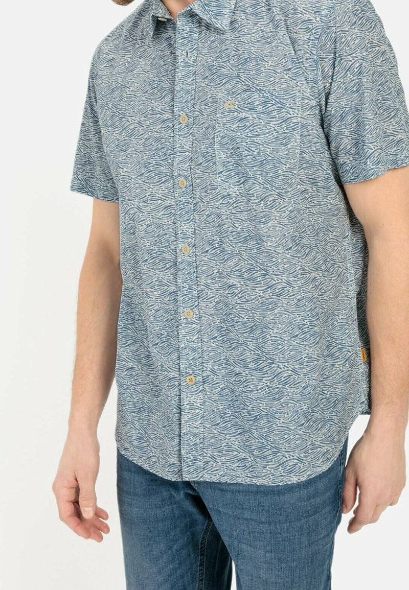 Camisa de manga corta en azul claro con patrón de olas, con botones en la parte delantera, cuello y bolsillo en el pecho. Fabricada con un tejido de textura suave.