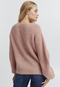 Maglione rosa a maglia con un fit morbido, maniche ampie e texture a coste. Presenta una schiena bassa e un aspetto morbido e accogliente.