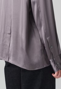 Zijde langarmshirt in een gedempt lavendelkleur met een zachte textuur, voorzien van een knoopsluiting bij de manchetten en een zijsplit aan de zoom.