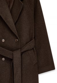 Divkāršu brūns vilnas mētelis ar lieliem atlokiem, horizontālām kabatām un atbilstošu jostu. Mīksta tekstūra ar maziem pogām kā akcentiem.