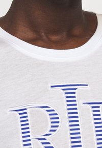 Vit bomull t-shirt med blå randiga broderade bokstäver "R" och "L". Rund hals med en mjuk textur och kort ärmdesign.