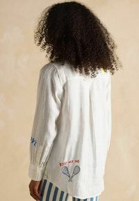 Valge pika varrukaga särk, millel on sinise ja punase tikandiga tekst "LOVE" ja "KISS MY ACE" ristatud tennise reketite paaril tagaosas.