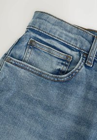 Světle modré džíny z denimu s vybledlým vzhledem, obsahující malou přední kapsu, viditelné švy a kovové detaily.