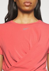 Camiseta Nike rosa con cuello redondo y mangas cortas. Presenta un sutil logo de Nike en gris en el pecho. Textura de tela suave y lisa.