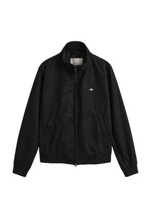 Zwarte jas met rits, opstaande kraag, zijzakken, elastische manchetten en een klein wit geborduurd logo op de linkerborst.