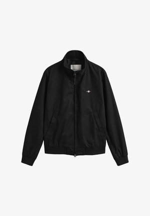 Zwarte jas met rits, opstaande kraag, zijzakken, elastische manchetten en een klein wit geborduurd logo op de linkerborst.