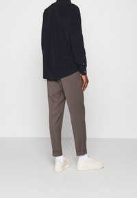Chemise marine à manches longues avec poignets à boutons, assortie à un pantalon marron ajusté ; baskets blanches à surface lisse et à lacets.