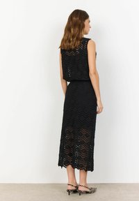Abito midi in pizzo nero con motivo a zigzag, design senza maniche e orlo a scallop. Abbinato a tacchi a righe nere e bianche.