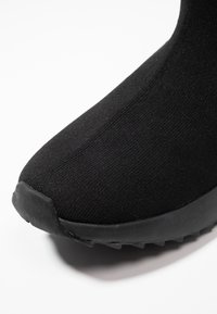 Black textile ankle boot with a sleek design, featuring a smooth knit upper, rubber sole, and textured accents on the toe.