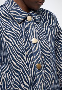 Μπλε και εκρού ζακάρ μπουφάν από κοτλέ με σχέδιο ζέβρας, γιακά και στρογγυλά χρυσά κουμπιά, που αναδεικνύουν την υφή και το σχέδιο.