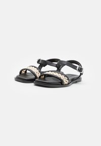 Sandales plates noires avec une bride en textile beige tressé, tige en cuir, deux brides de cheville ajustables et semelle lisse.