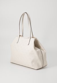 Sac fourre-tout blanc avec un motif floral en relief, texture lisse et bordure brune contrastante. Dispose de deux poignées robustes et ergonomiques pour un transport facile.