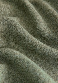 Strukturiertes Gewebe in gedämpften Grüntönen, das eine weiche, leicht flauschige Oberfläche mit einem gewebten Muster und natürlichen Farbvariationen aufweist.