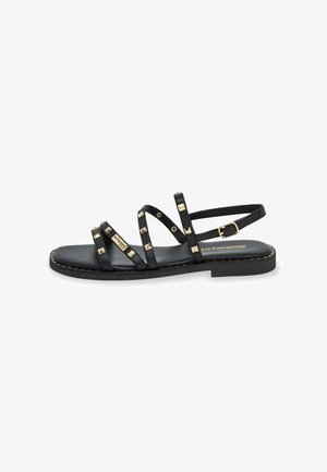 Black flat sandals featuring multiple thin straps adorned with metallic gold studs, a buckle closure, and a smooth leather sole.