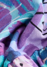 Gros plan sur un tissu doux avec des motifs abstraits vibrants en violet, bleu et teal, présentant une texture tricotée visible, montrant des plis et des creux.