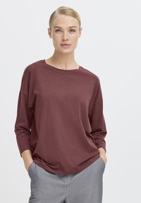 Bordeauxrotes Langarmshirt mit rundem Halsausschnitt, lockerer Passform und weicher Textur, kombiniert mit grauen, taillierten Hosen.