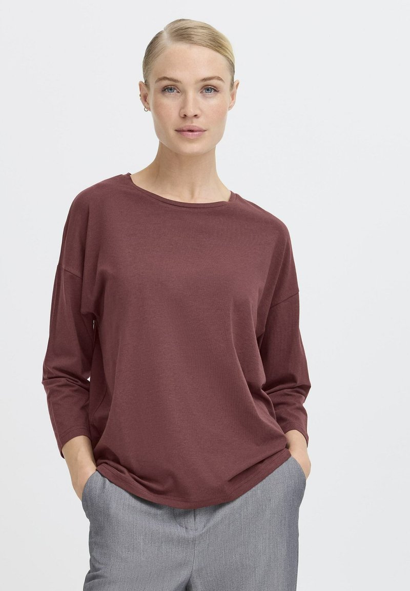 Bordeauxrotes Langarmshirt mit rundem Halsausschnitt, lockerer Passform und weicher Textur, kombiniert mit grauen, taillierten Hosen.