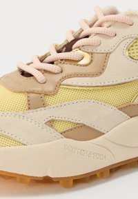 Shoe: cream and yellow sneaker with mesh and suede panels, pink laces, prominent sole, and logo detail on the side.