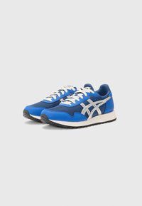 Baskets de sport bleues en combinaison de maille et de matériaux synthétiques, avec des lacets blancs, des accents argentés, et une semelle en caoutchouc texturée.
