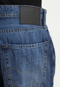 Jeans in denim blu scuro con un'etichetta in pelle in vita e classici motivi di cucitura, dotati di un design per la tasca posteriore.