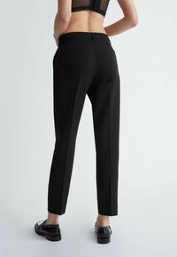 Pantaloni neri su misura con un design a gamba dritta, dotati di due tasche posteriori e una texture liscia, abbinati a mocassini neri.