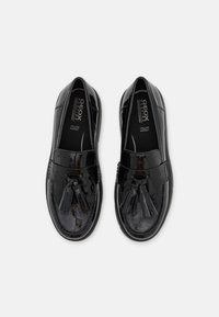 Mocassins en cuir verni noir avec une finition lisse, dotés d'un accent à frange et d'une semelle intérieure rembourrée pour plus de confort.