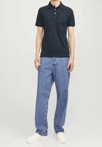 Námořnická polo košile s malým červeným logem, spárovaná se světle modrými volnými džíny a bílými teniskami. Hladký materiál a volný střih.