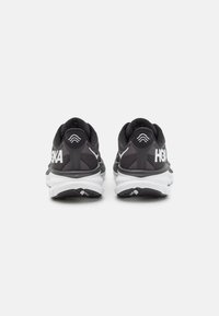 Scarpe da atletica nere con tomaia in rete testurizzata e suola bianca. Presentano il marchio HOKA sul tallone, offrendo un design elegante e aerodinamico.