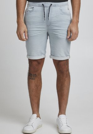 Shorts en jean bleu clair, taille élastique avec cordon de serrage, ourlet roulé, deux poches avant, texture lisse, portés avec des baskets blanches.