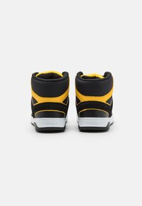 Sneakers înalte cu o gamă de suede negru și accente galbene, având un guler căptușit, o talpă intermediară albă și o talpă exterioară din cauciuc texturat.