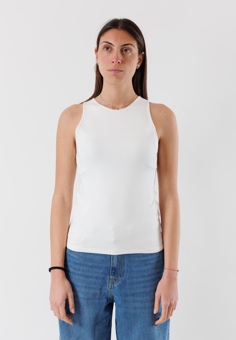 Top bianco senza maniche con collo rotondo, realizzato in tessuto liscio. Presenta un design aderente e una leggera arricciatura ai lati, abbinato a jeans blu.