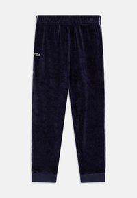 Pantaloni de trening velur bleumarin cu talie elastică și manșete cu nervuri, având un logo brodat verde pe partea stângă.